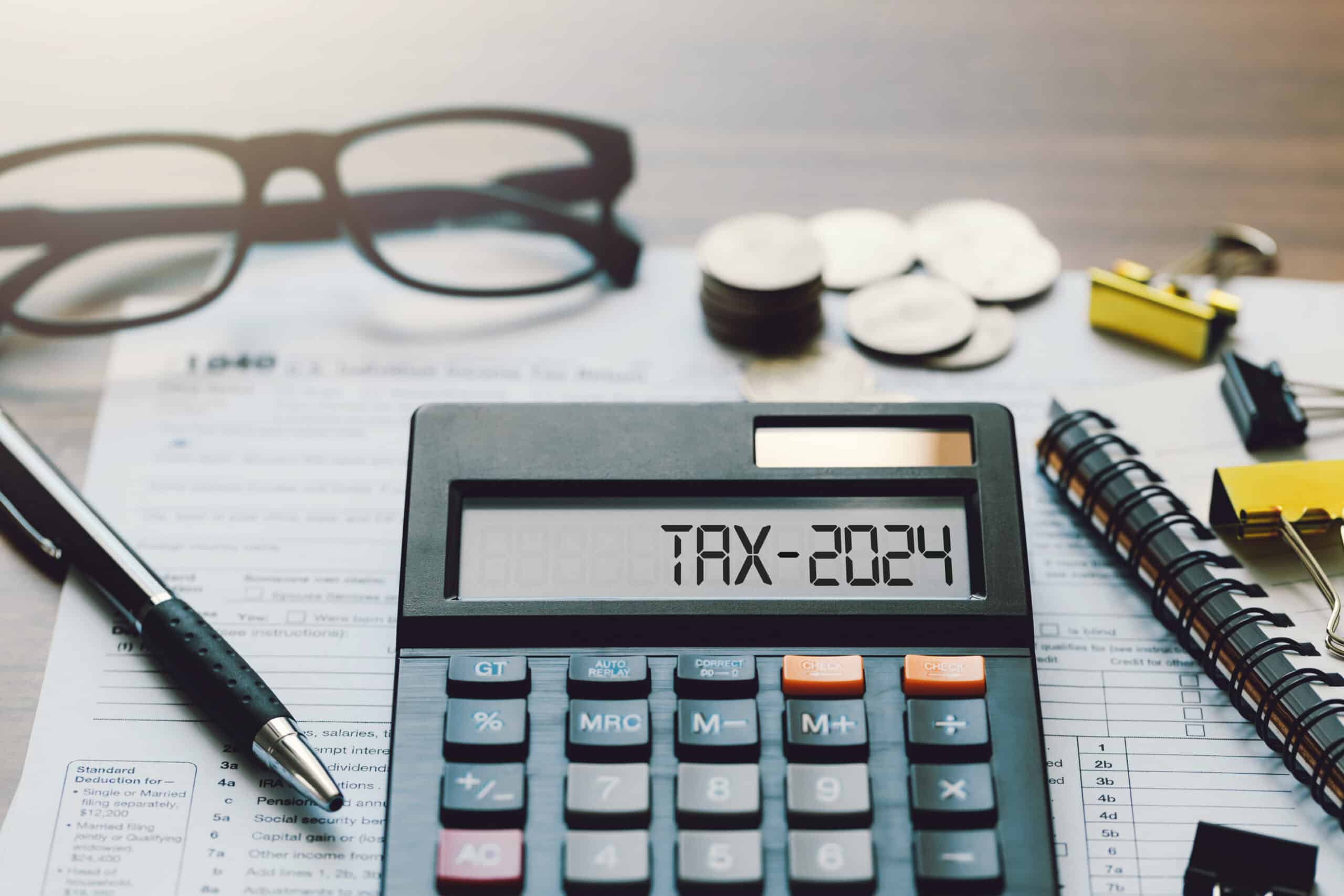 Word Tax 2024 on the calculator. Business and tax concept.Calculator, coins, book, tax form, and pen on table.Tax deduction planning.Financial research, government taxes, and calculation tax return